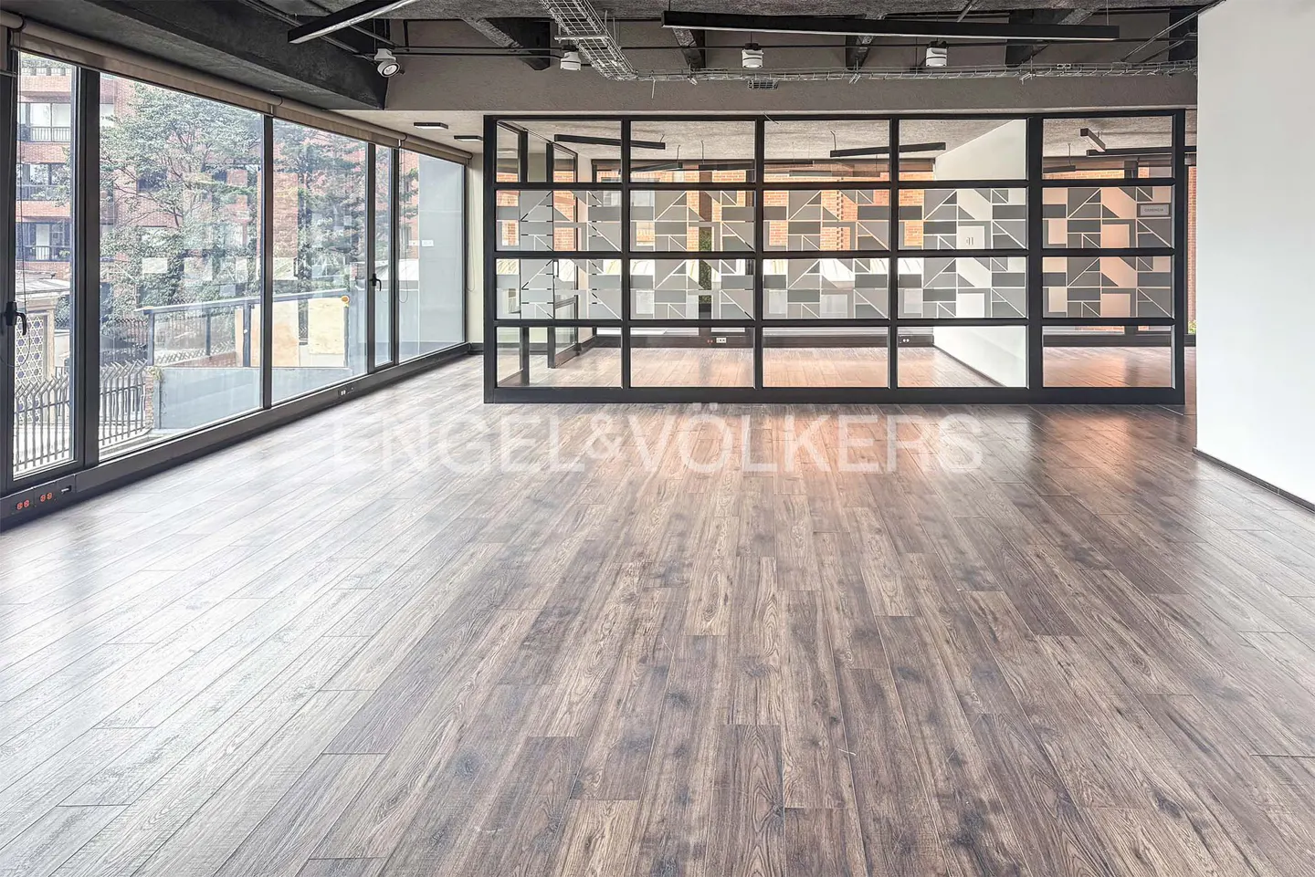 Empty office space with wood floors, large windows, and a glass-enclosed room with geometric patterns.