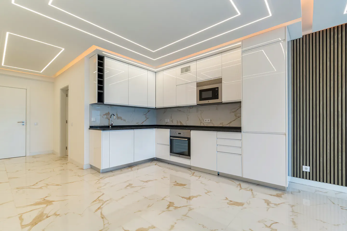 Modern kitchen with white glossy cabinets, marble-patterned backsplash and floor, built-in oven, and LED ceiling lighting.