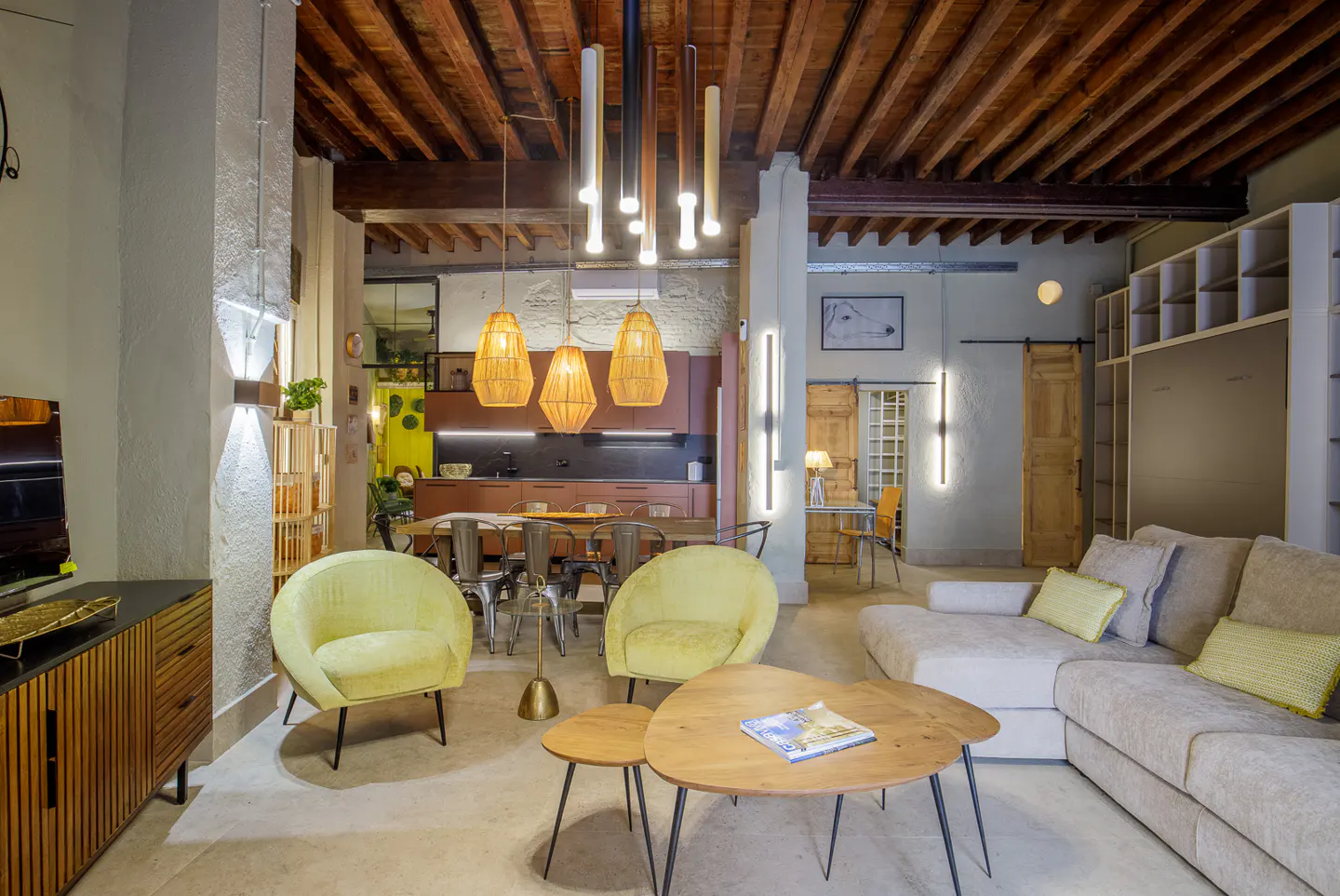 Living room with yellow chairs, wooden table, and beige sofa. The ceiling has wooden beams and modern lighting fixtures.