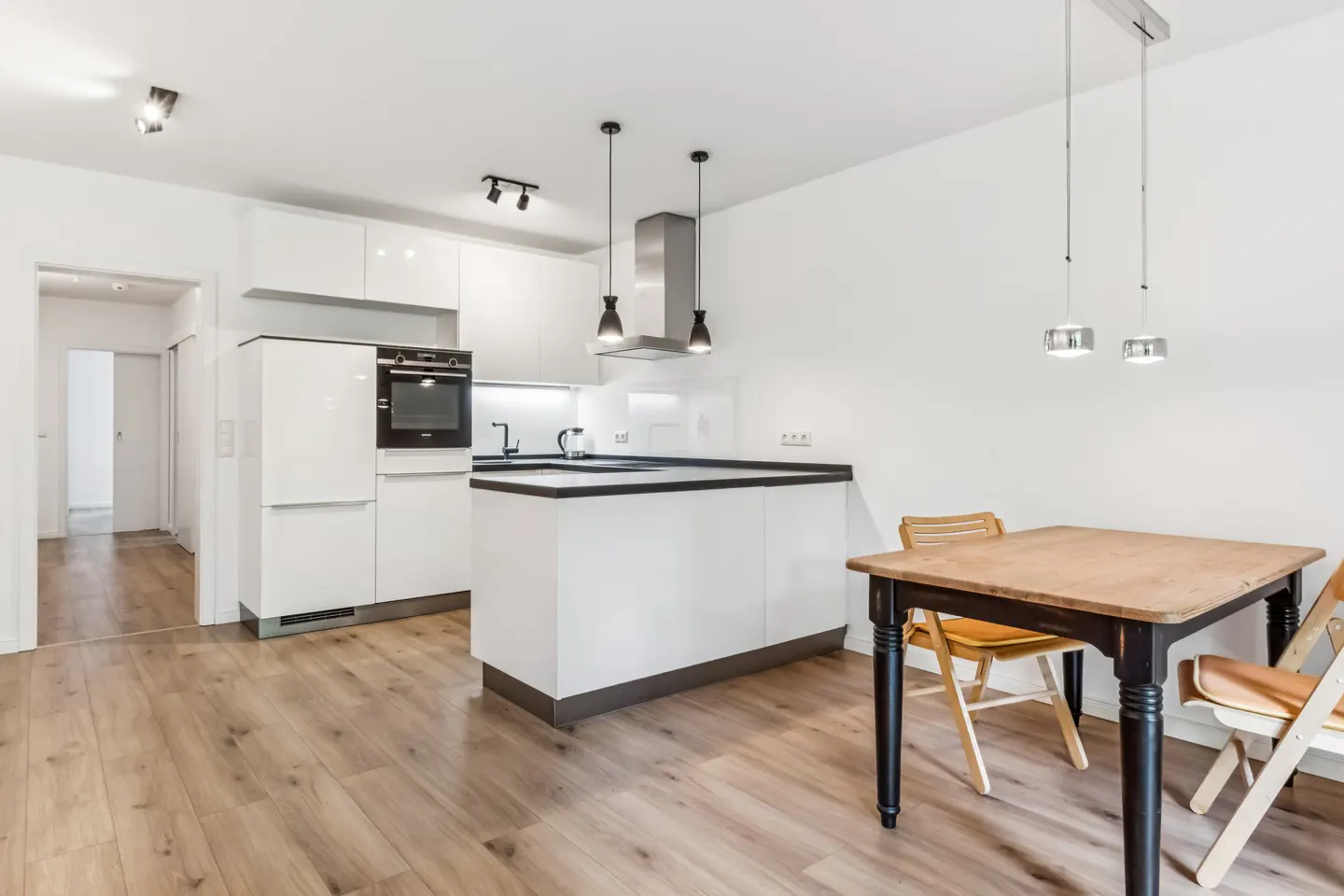 Bright, modern kitchen with white cabinets, black countertops, and wood floors. A wooden table with chairs sits nearby.