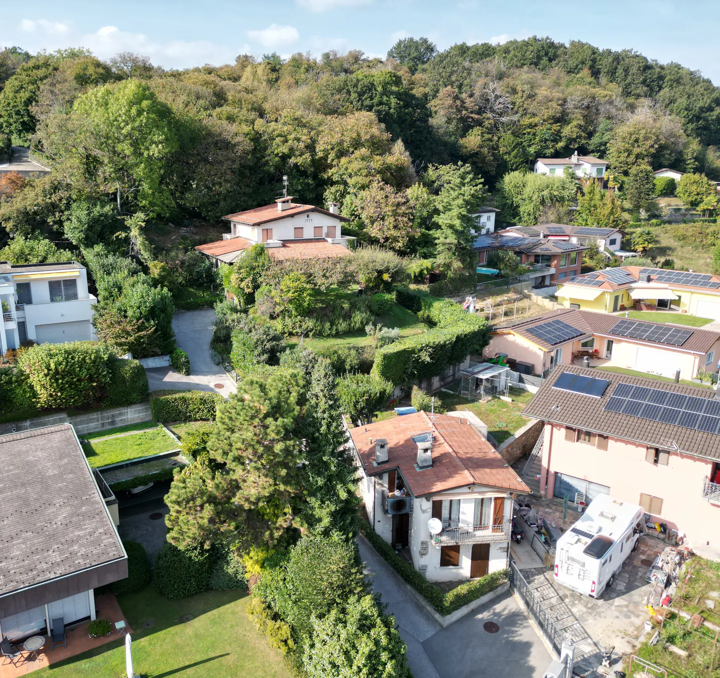 Aerial view of houses nestled in a green, wooded hillside neighborhood on a sunny day.