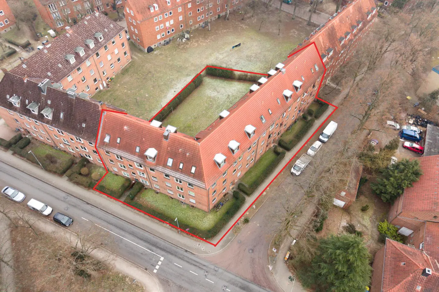 Aerial view of a brick apartment complex with a red outline, surrounding a grassy courtyard. Cars are parked along the street.