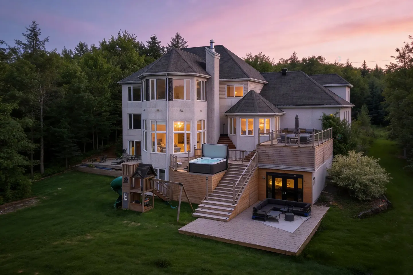 A large, white house with a hot tub and deck, surrounded by green trees under a pink and purple sky.