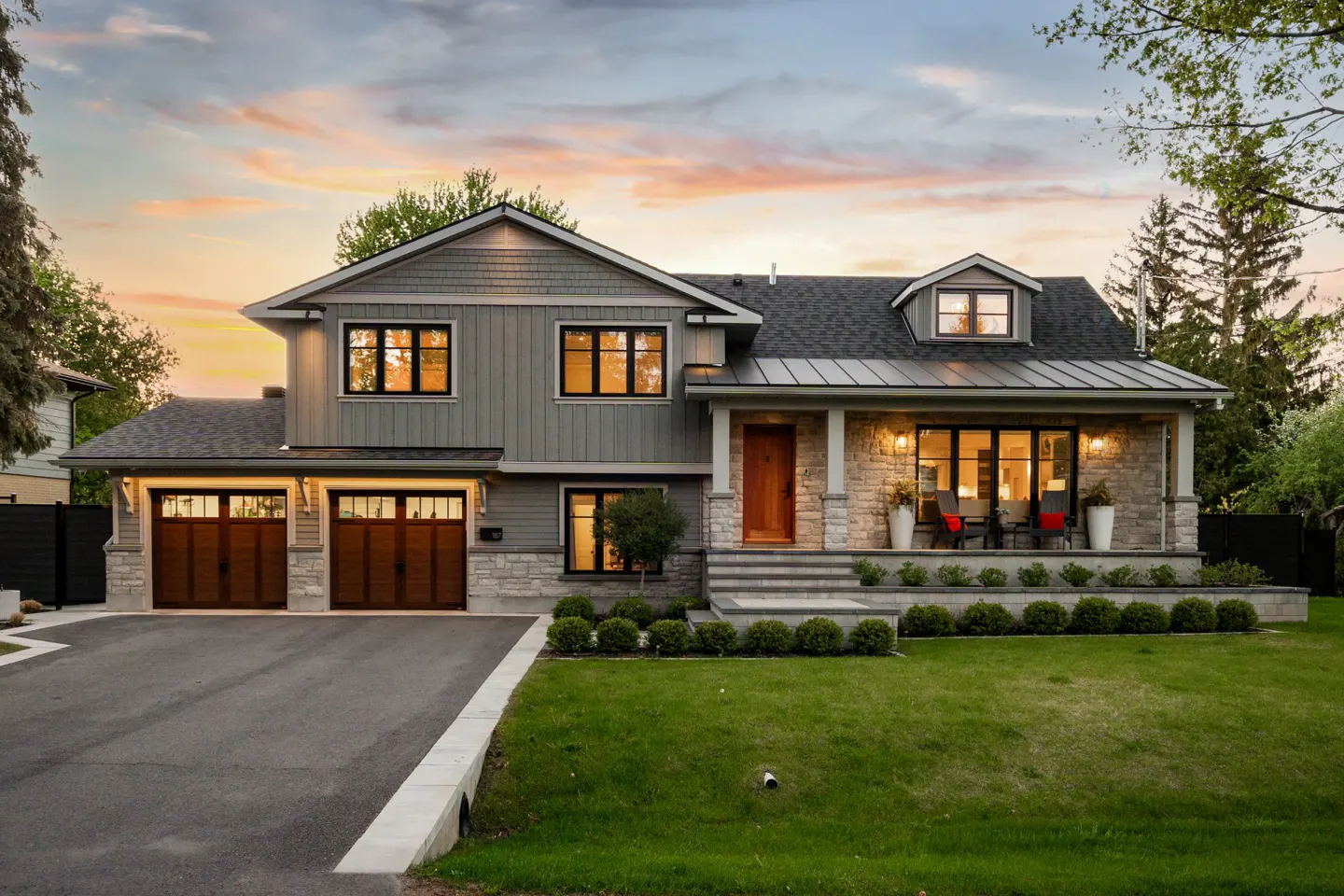 Two-story house with gray siding, stone accents, and a dark roof. A green lawn and driveway lead to the two-car garage.