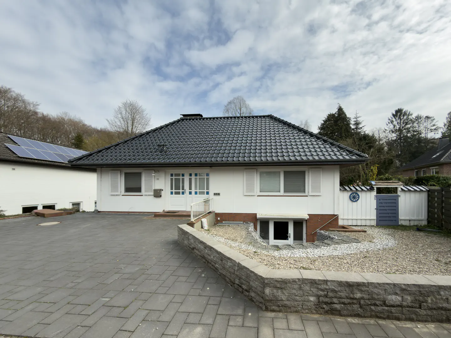 A white, one-story house with a dark gray roof and a paved driveway on a cloudy day.