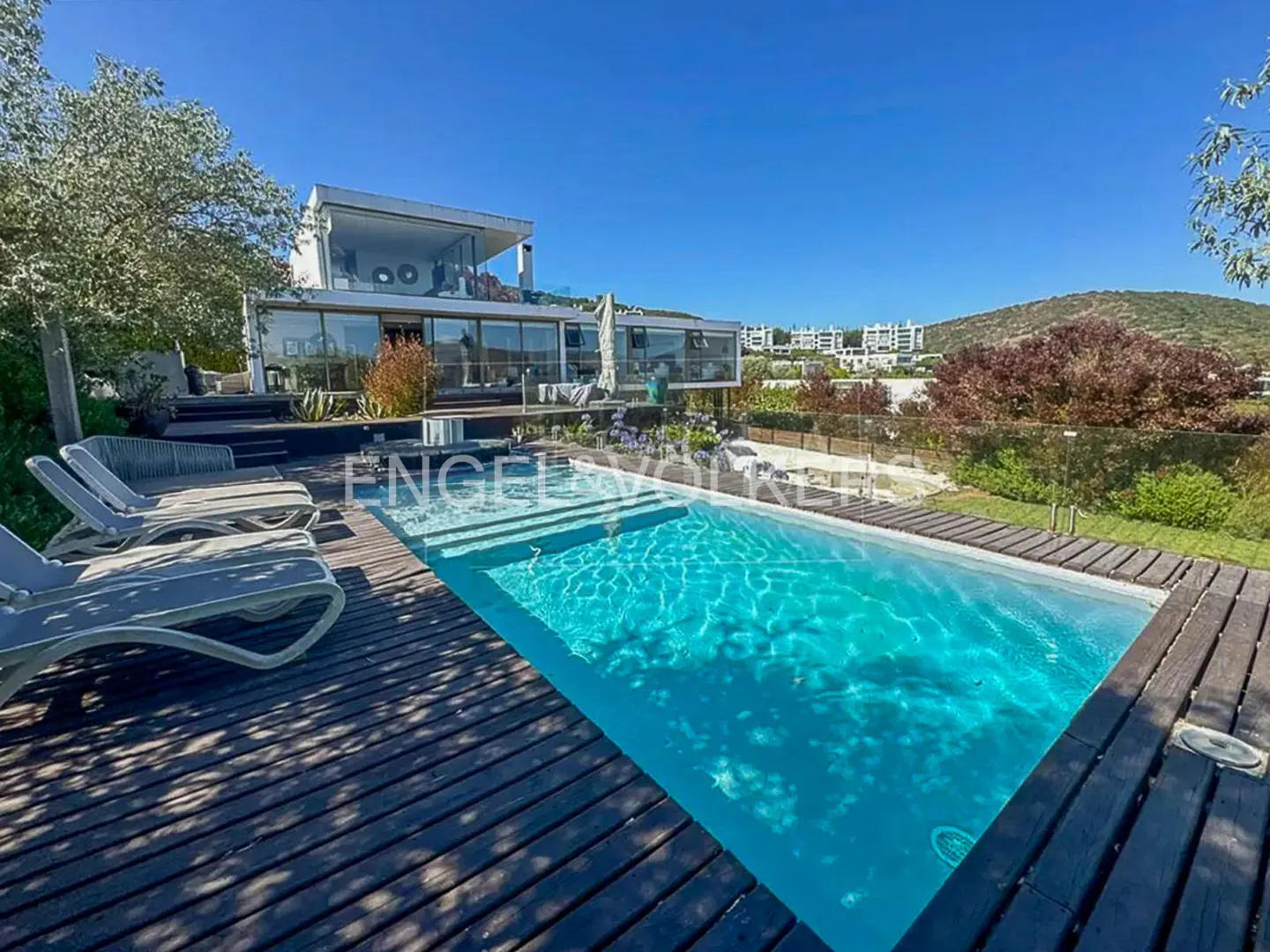 A modern white house with a pool and lounge chairs on a sunny day.