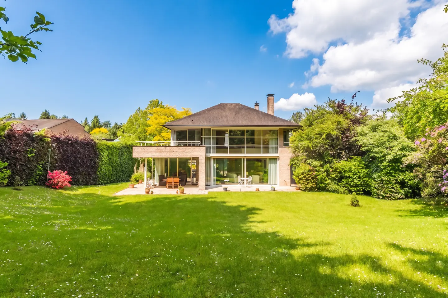 Two-story house with large windows, a brown roof, and a green lawn on a sunny day.