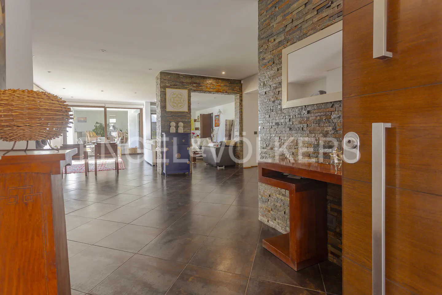 Modern entryway with dark tile floors, a stone accent wall, a wooden console table, and an open-concept living area beyond.