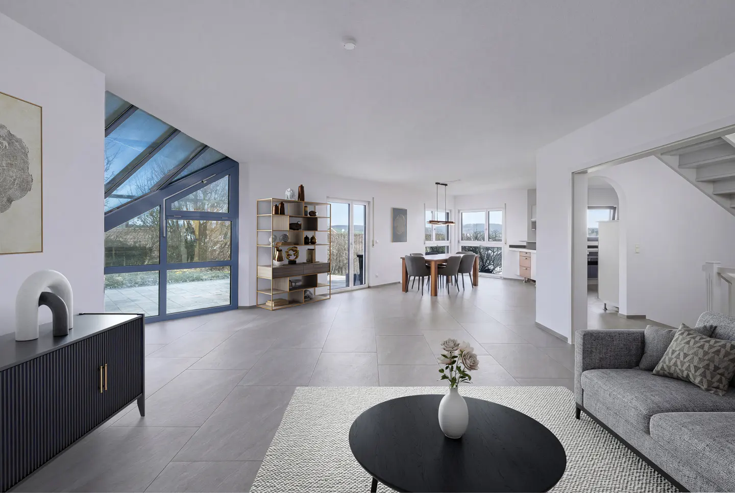 Bright, open-concept living space with gray tile flooring, a black coffee table, and a gray sofa. Large windows offer outdoor views.