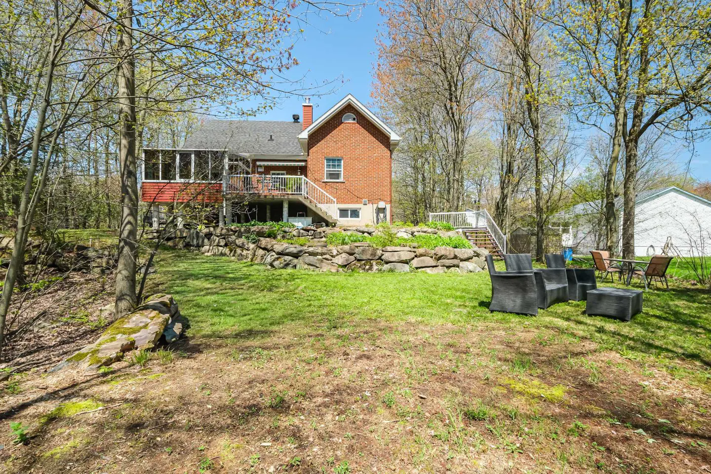 Backyard view of a red brick house with a stone retaining wall and outdoor seating.