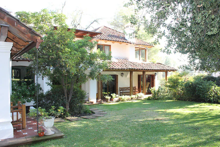 Two-story white house with a red tile roof, wooden porch, and green lawn.