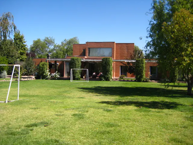 Brick house with a large green lawn, trees, and two soccer goals under a clear blue sky.