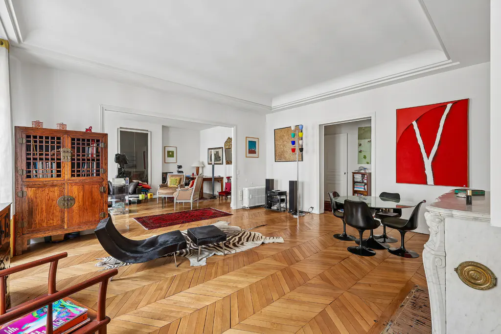 Wide shot of a bright, open-concept living and dining area with parquet floors and eclectic decor.