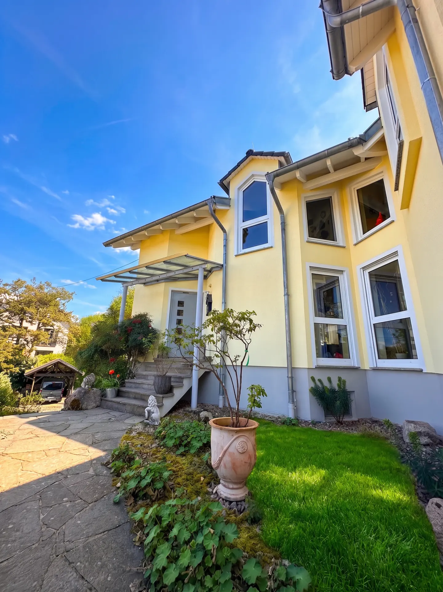 Exterior of a yellow two-story house with white trim, a glass awning, and a stone walkway leading to the front door.