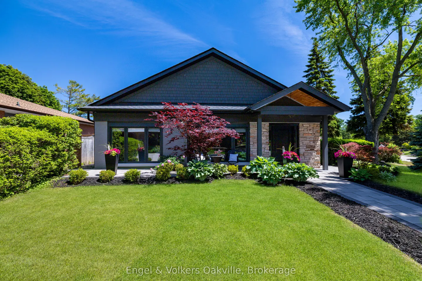 Modern bungalow with dark grey siding, stone accents, a red Japanese maple, and a manicured lawn under a clear blue sky.