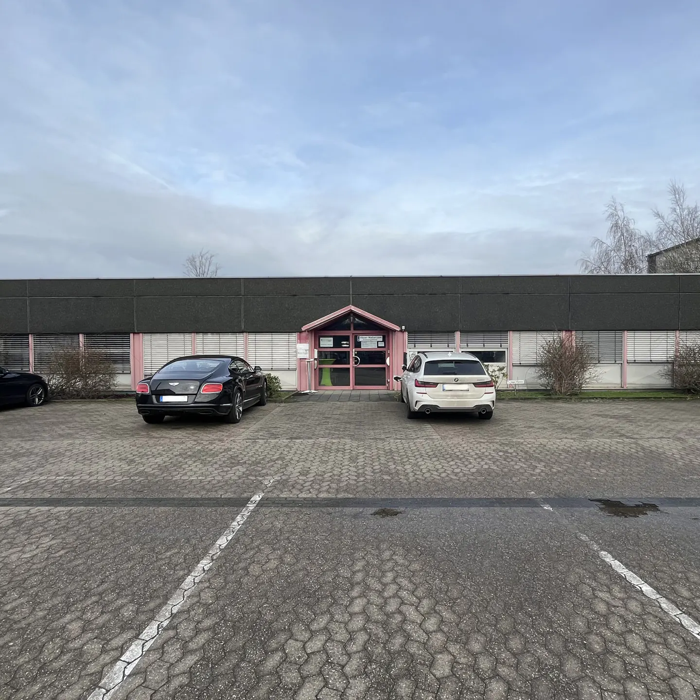 Building with a pink entrance and two parked cars. A black Bentley is on the left and a white BMW is on the right.