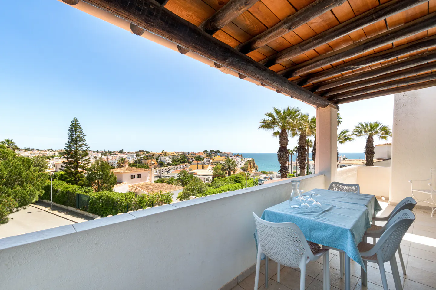 Balcony with table set for four, blue tablecloth, ocean view, palm trees, and a blue sky.