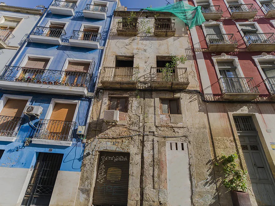 Three colorful buildings stand side-by-side. The left is blue, the center is weathered, and the right is red and white. Each has balconies.