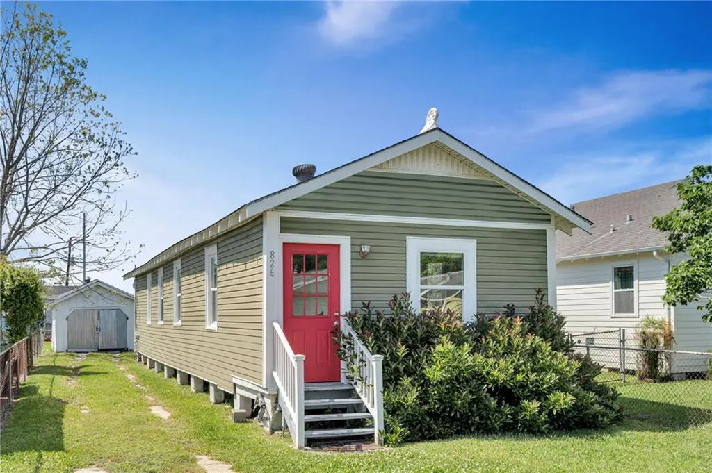 Exterior view of a green house with a red door, white trim, and a small front yard.