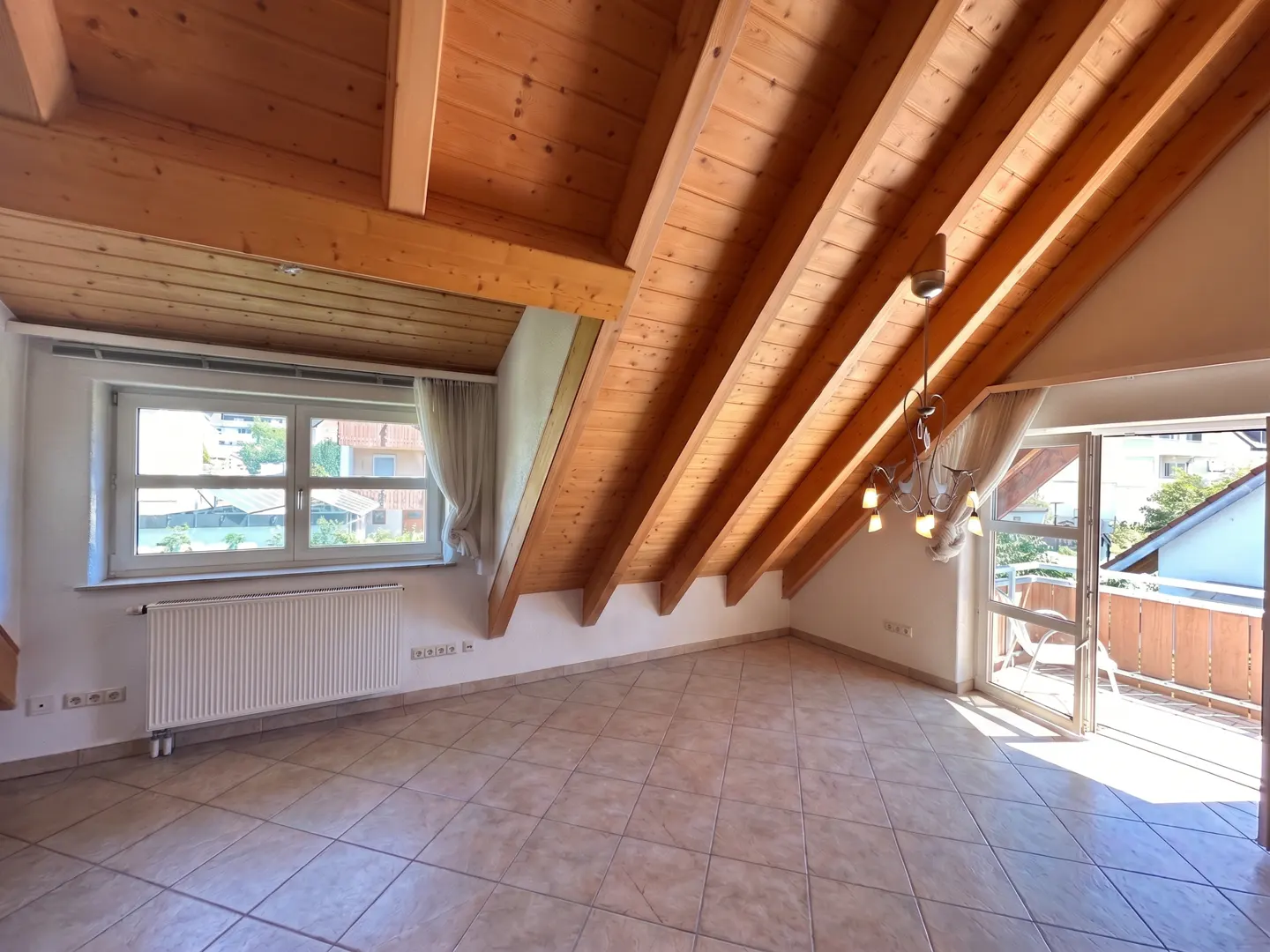Attic room with wood-paneled ceiling, tile floor, window, radiator, and balcony access with outdoor seating.