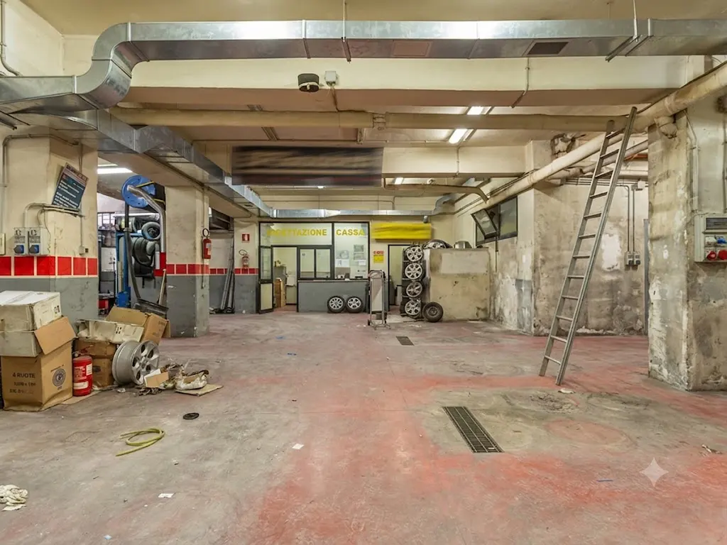 Spacious industrial garage with red concrete floors, exposed ceiling ducts, a metal ladder, and a small office area.