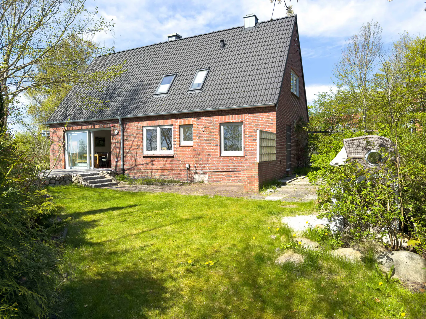 A red brick house with a gray roof and a green lawn on a sunny day.