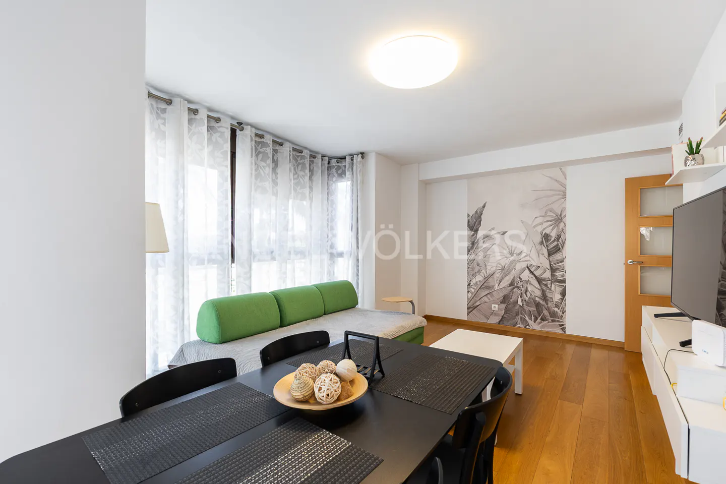 Living room with a green sofa, black table, and wood floors. A tropical mural is on the wall.