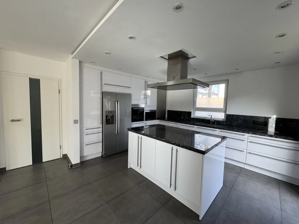A modern kitchen with white cabinets, black granite countertops, and stainless steel appliances. A central island stands on gray tile flooring.