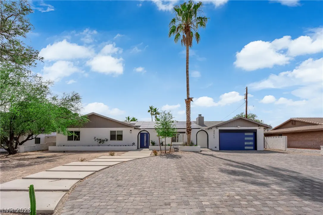 Single-story white home with a blue front door and garage, a tall palm tree, and a paved driveway under a blue sky.