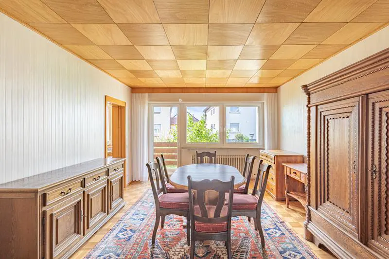 A dining room with wood furniture, a patterned rug, and a checkered wood ceiling.