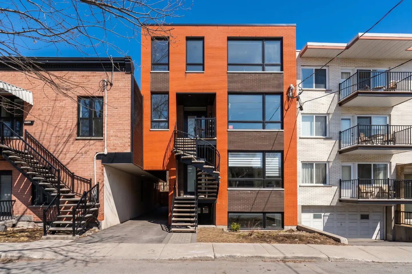 A three-story orange brick building with a black spiral staircase in front. Other buildings are on either side.