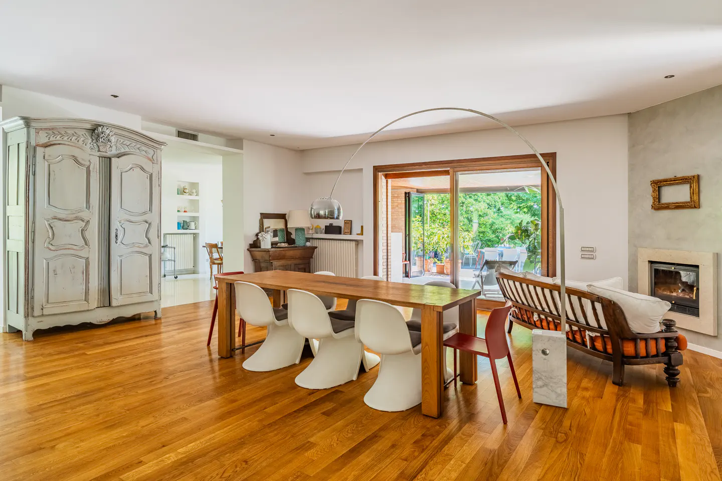 Bright living room with wood floors, a long table with white chairs, and a vintage armoire. Sliding glass doors lead to a patio.