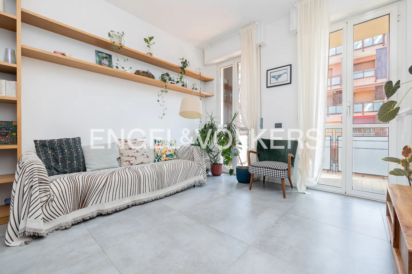 Bright living room with a striped couch, shelves with plants, and a green chair near a window.