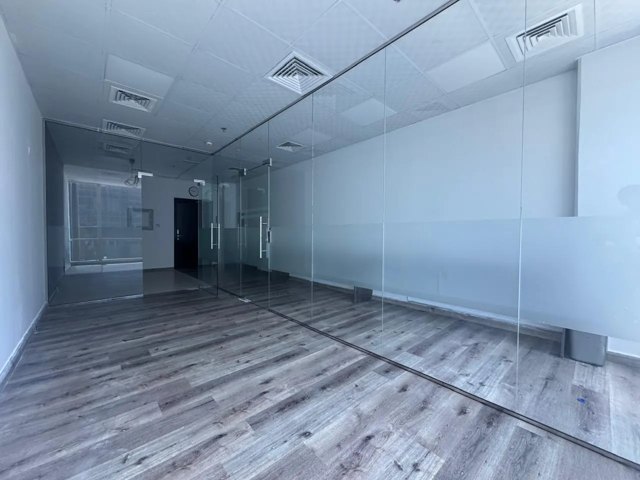 Empty office space with wood-look floors, white walls, and glass-walled rooms.