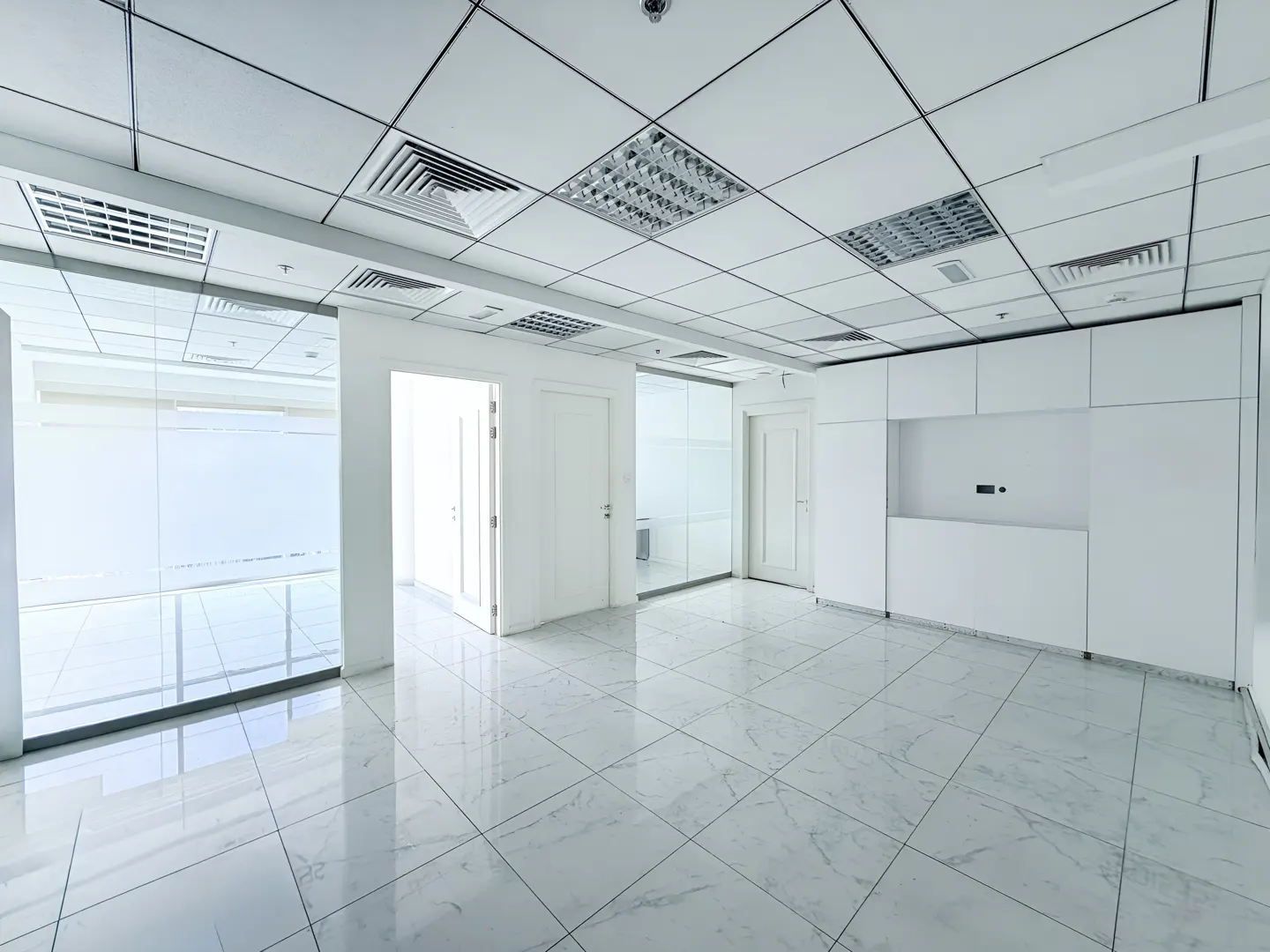 Bright, empty office space with white walls, tiled floor, and glass-walled rooms.