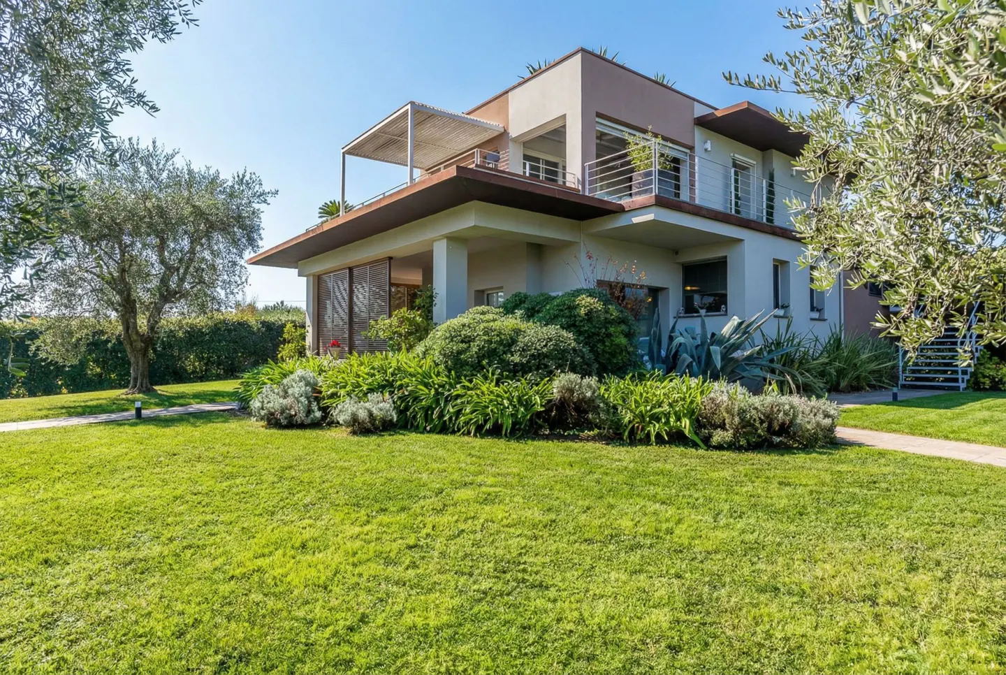 Two-story house with a brown roof, white walls, and a green lawn in front of it.