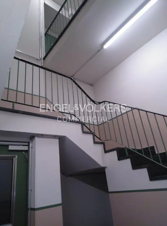 Interior view of a stairwell with black metal railings and white walls. A green door is visible on the left. The Engel & Völkers logo is superimposed.