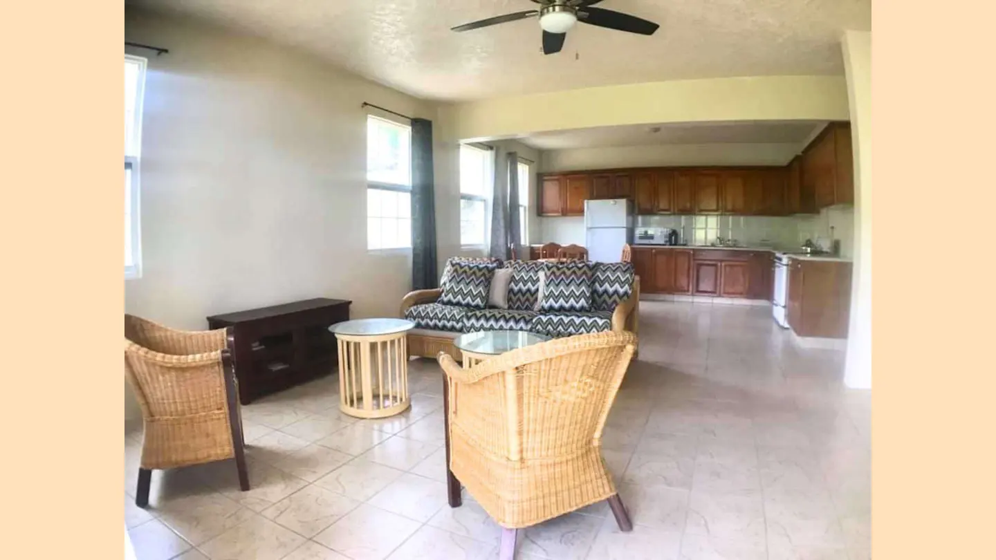 Open-concept living area with wicker chairs, patterned sofa, and wooden kitchen cabinets on a tiled floor.