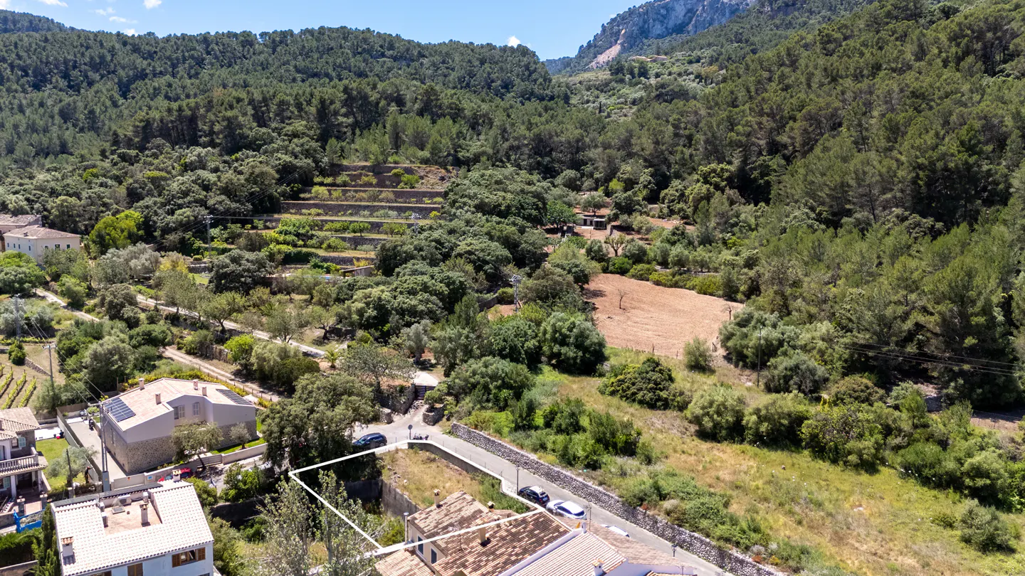 Aerial view of a property with a white outline, surrounded by lush green trees and mountains in the background.