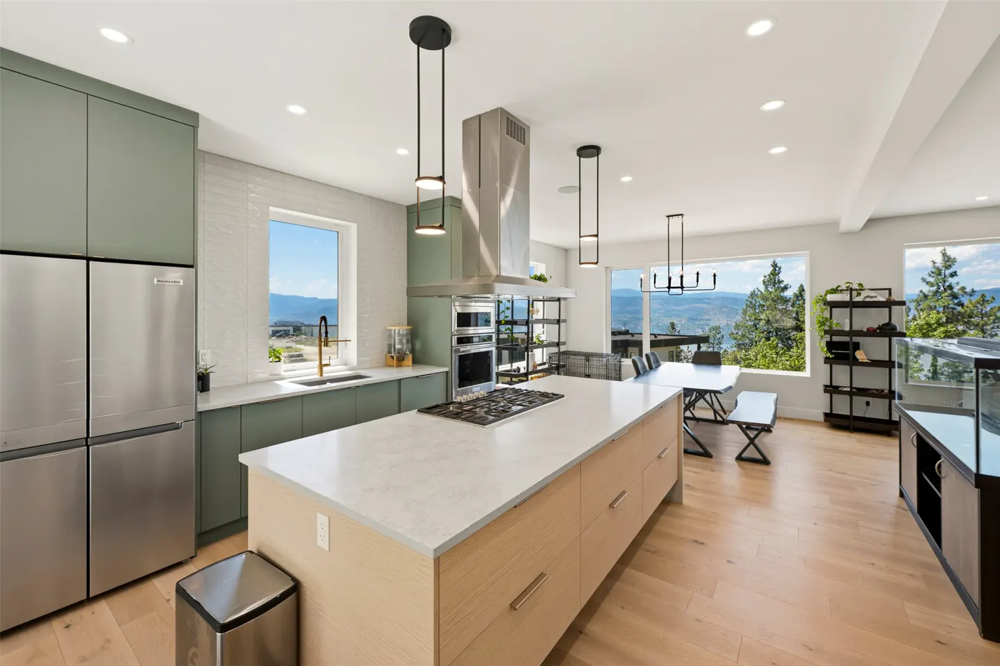 Modern kitchen with sage green cabinets, light wood island, stainless steel appliances, and large windows with mountain views.