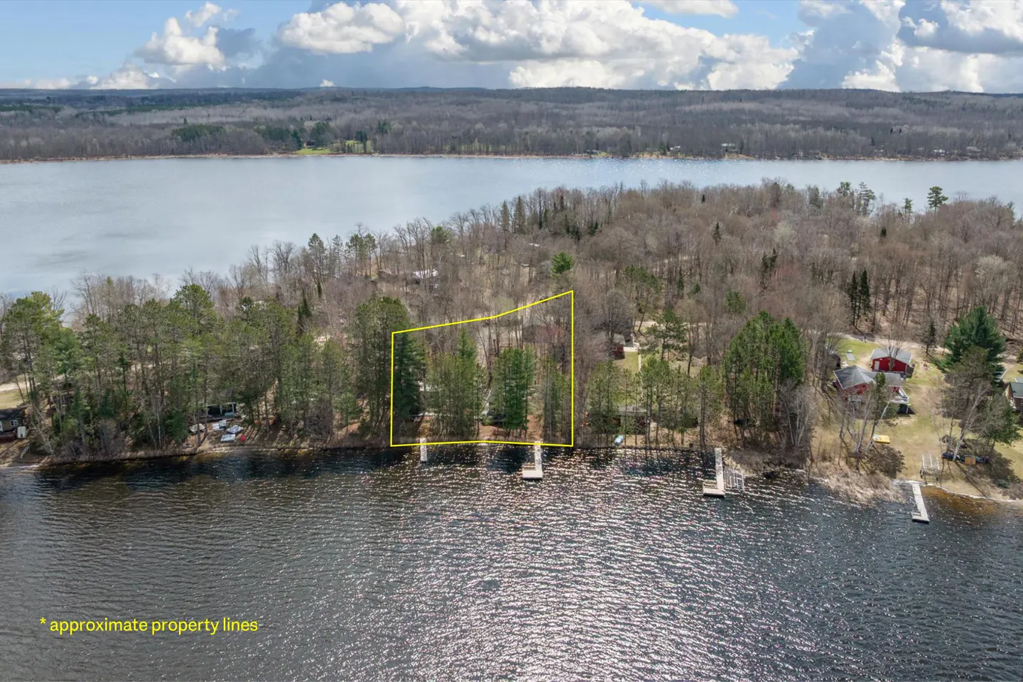Aerial view of a wooded lakefront property outlined in yellow, with docks and blue water.