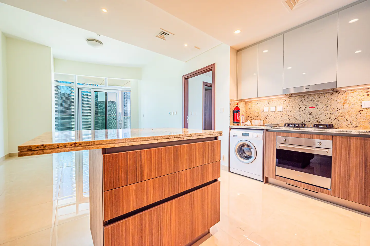A modern kitchen with a wood island, white cabinets, and stainless steel appliances. A washing machine is next to the oven. A balcony with city views is visible.