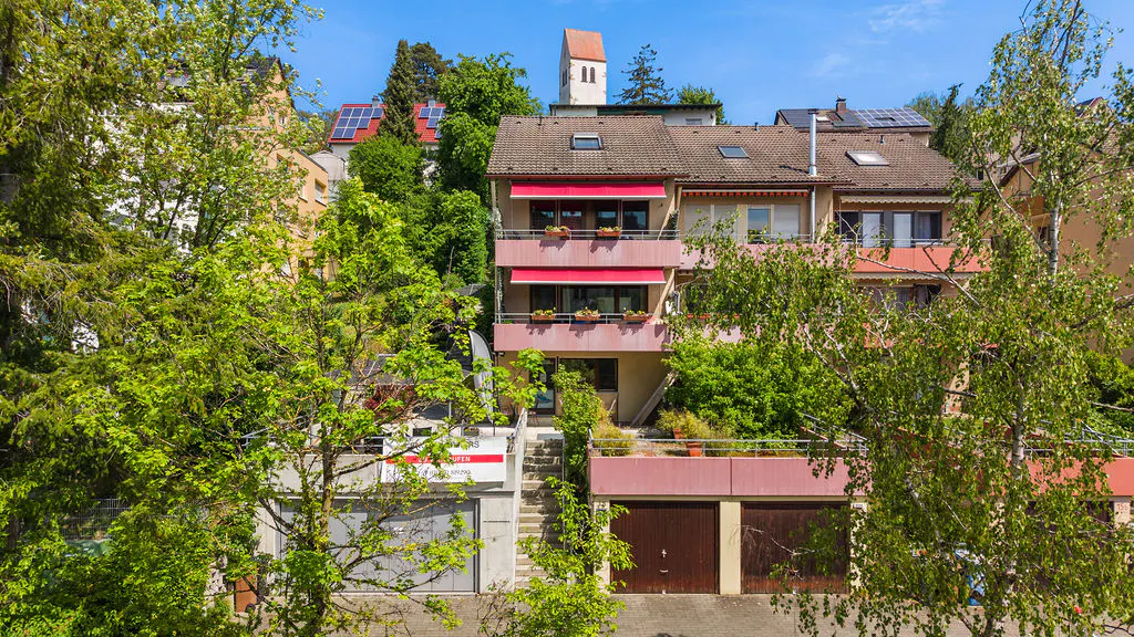 Three-story pink apartment building with red awnings and brown garage doors, surrounded by green trees.