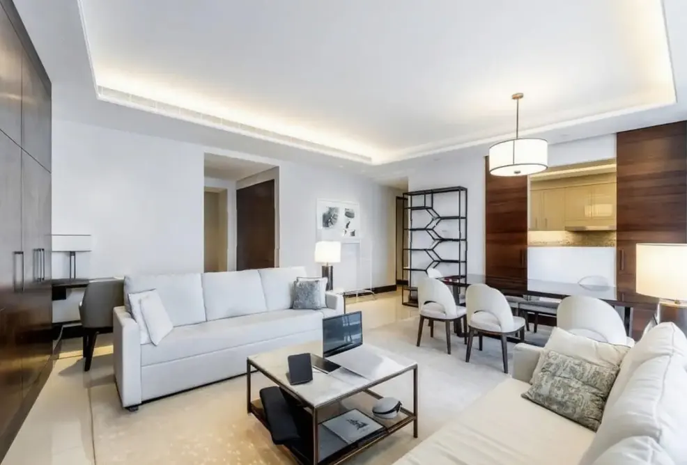 Modern living room with white sofas, a marble coffee table, dark wood accents, and a dining area with white chairs.