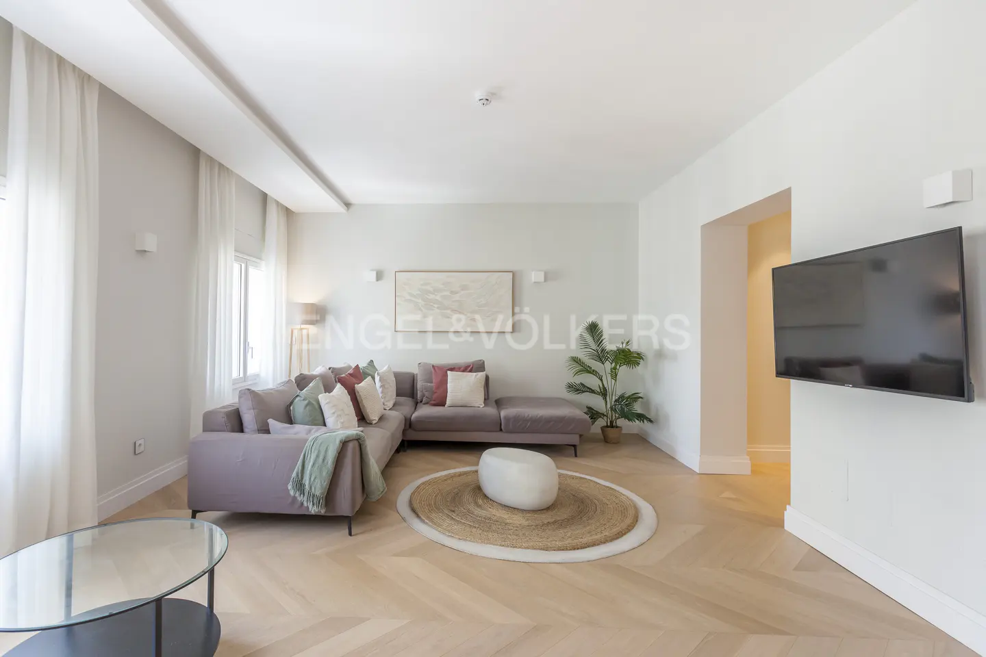 Living room with a gray sectional sofa, pillows, a round rug, and a TV on the wall.