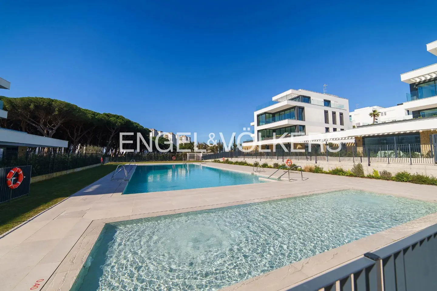 Exterior view of a modern white building with a pool and Engel & Völkers logo under a clear blue sky.