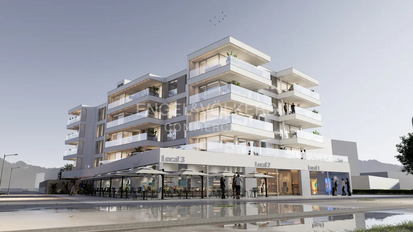 Modern white building with glass balconies and commercial spaces below. People are visible on balconies and in front of shops.