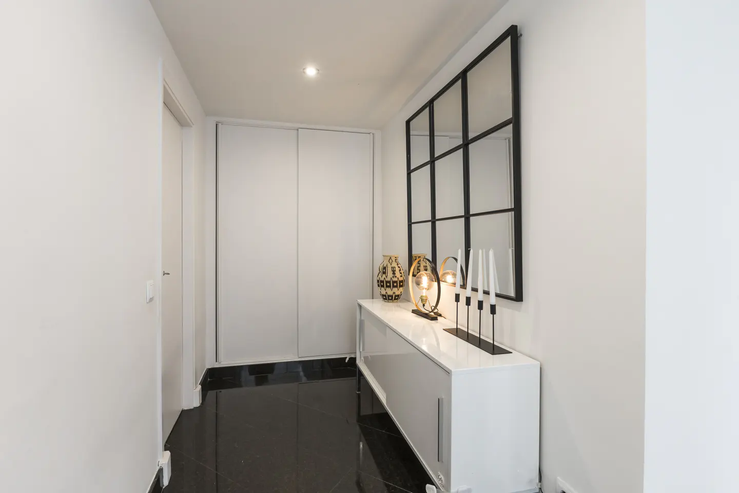 Hallway with black tile floor, white walls, and a white cabinet with decor under a black framed mirror.