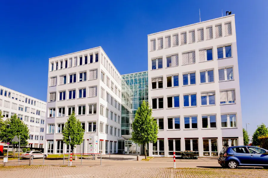 Modern white office building with a glass atrium under a clear blue sky.