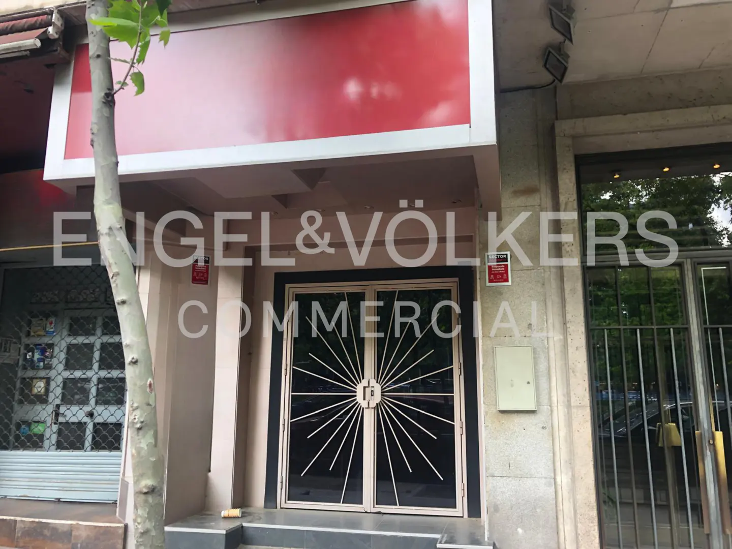 Exterior of a commercial building with a red sign and decorative metal doors. The Engel & Völkers logo is superimposed on the image.